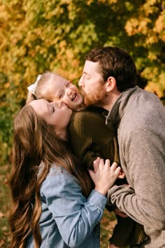 a man and woman kissing each other while standing in front of trees with yellow leaves