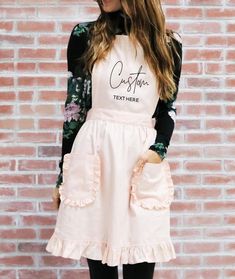 a woman standing in front of a brick wall wearing a white apron and black tights