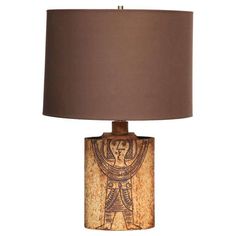 a table lamp with an egyptian design on the base and a brown shade over it