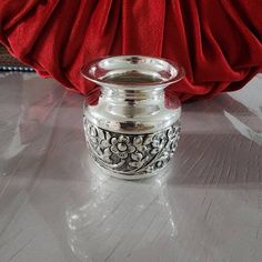 a silver vase sitting on top of a table next to a red cloth covered wall