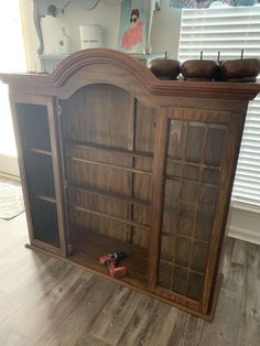 an old wooden cabinet with glass doors and drawers on the bottom shelf, in front of a window