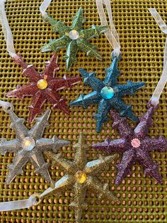 five glittered star ornaments are on a mesh tablecloth with white ribbon around them