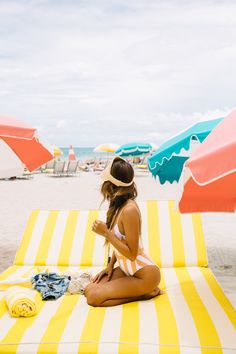 a woman sitting on top of a yellow and white striped beach towel next to an umbrella