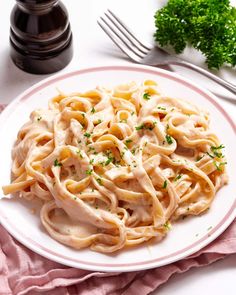 a white plate topped with pasta covered in sauce and garnished with parsley