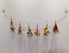 several pieces of art hanging on a string in front of a white wall with flowers attached to it