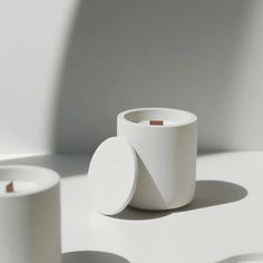 two white cups sitting next to each other on a table with shadows from the wall behind them