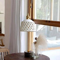 a white lamp hanging over a wooden table in front of a window with drapes