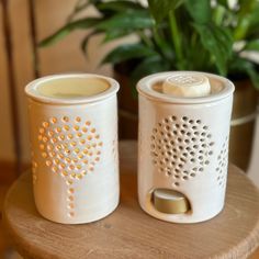 two white canisters sitting on top of a wooden table next to a potted plant