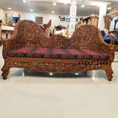 an ornately carved wooden couch sits in a room with white tile flooring and walls