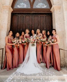 a group of women standing next to each other in front of a wooden door holding bouquets