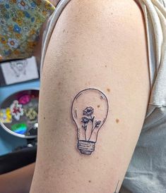 a woman with a tattoo on her arm has a light bulb and flowers in it