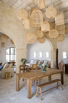 a dining room table surrounded by hanging wicker lamps and chairs in front of a stone archway