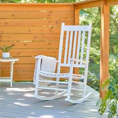 a white rocking chair sitting on top of a wooden deck next to a small table