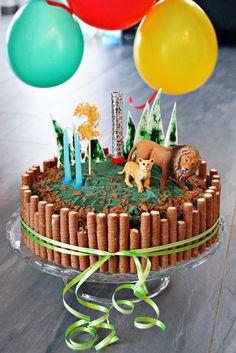 a birthday cake with candles and animals on it, surrounded by balloons in the background