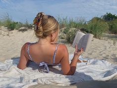 a woman reading a book on the beach while sitting in the sand with her back to the camera