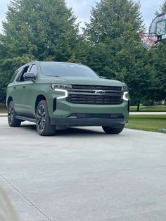 a green chevy suv parked in front of a basketball hoop on a driveway with trees behind it