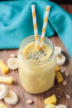 a smoothie in a mason jar with two striped straws on top and sliced bananas around it