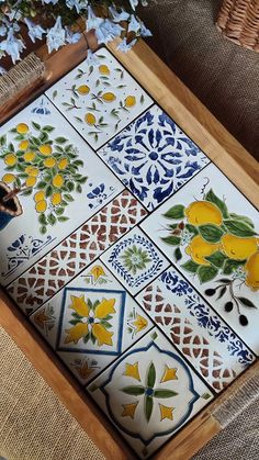 a wooden tray with yellow and blue tiles on it, next to a basket full of flowers