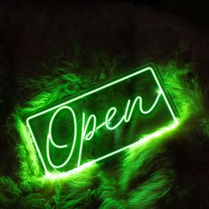 a neon sign that reads open on top of some green furry material in the dark