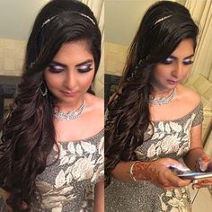 a woman with long dark hair is looking at her cell phone while wearing a silver dress