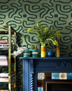 a room with a fireplace, bookshelf and vases filled with plants on the mantle