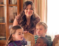 a woman sitting at a table with two children in front of her and another child eating cake