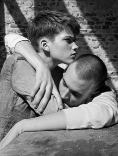 black and white photograph of two people embracing each other in front of a brick wall