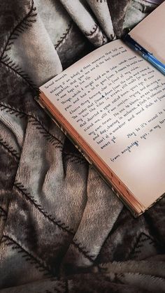 an open book laying on top of a bed next to a blue pen and pillow