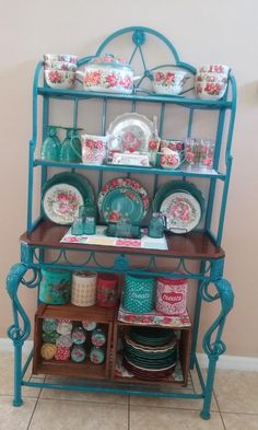 a teal china cabinet with plates and cups on it's shelf, next to a pink wall