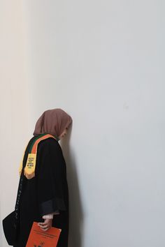 a person wearing a black jacket with a brown hood is standing against a white wall