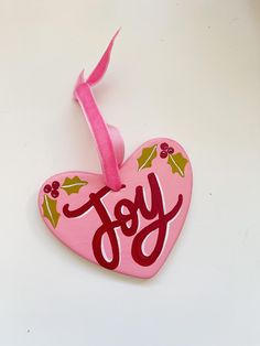 a pink heart shaped ornament with the word joy painted on it's side