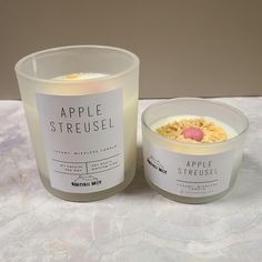 an apple streusel candle sitting next to a glass container on a marble table