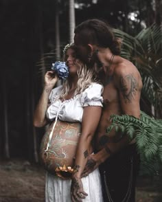 two people standing next to each other with tattoos on their arms and stomachs, one holding a pregnant woman's belly