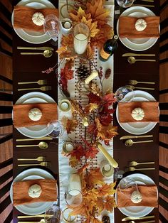 the table is set with white plates, silverware and autumn leaves on it's placemats