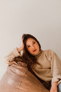 a woman sitting on top of a brown leather bag with her hands behind her head