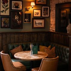 a corner table with two chairs and pictures on the wall above it in a restaurant