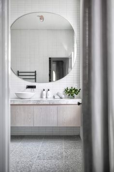 a bathroom with a large round mirror above the sink and white tiles on the walls