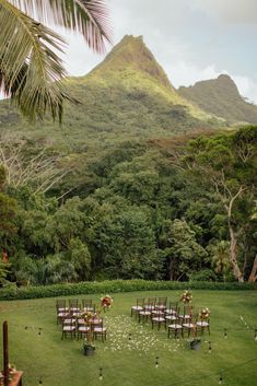 a lush green field with chairs and tables set up for an outdoor wedding in front of a mountain