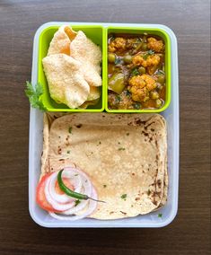 a plastic container filled with food on top of a wooden table next to a fork and knife