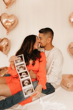 a man and woman cuddling on a bed with hearts hanging from the wall behind them