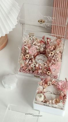 two white boxes with pink flowers in them on a table next to a paper fan