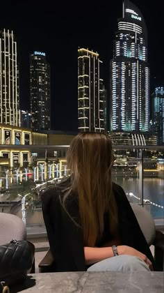 a woman sitting on top of a couch next to a window looking at the city