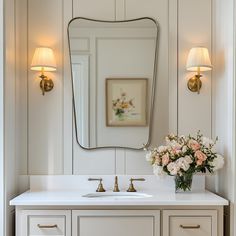 a bathroom vanity with two sinks and a large mirror above it, along with flowers in a vase on the counter