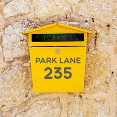 a yellow mailbox on the side of a stone wall that reads park lane 2235