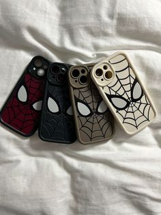 three cell phones with spider - man cases sitting on top of a white bed sheet