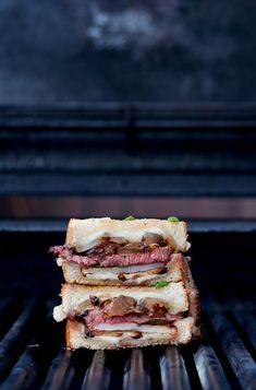 two sandwiches stacked on top of each other on a bbq grill with tongs