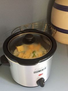 an electric crock pot with cheese and broccoli in it on a counter