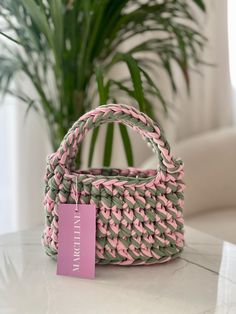 a pink and green woven bag sitting on top of a table next to a potted plant