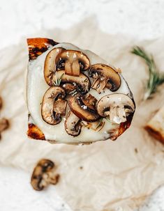 a slice of pizza with mushrooms on it being held up by a hand over a piece of parchment paper