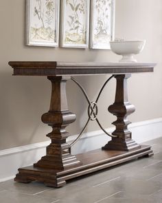 a wooden table with two pictures on the wall above it and a bowl sitting on top